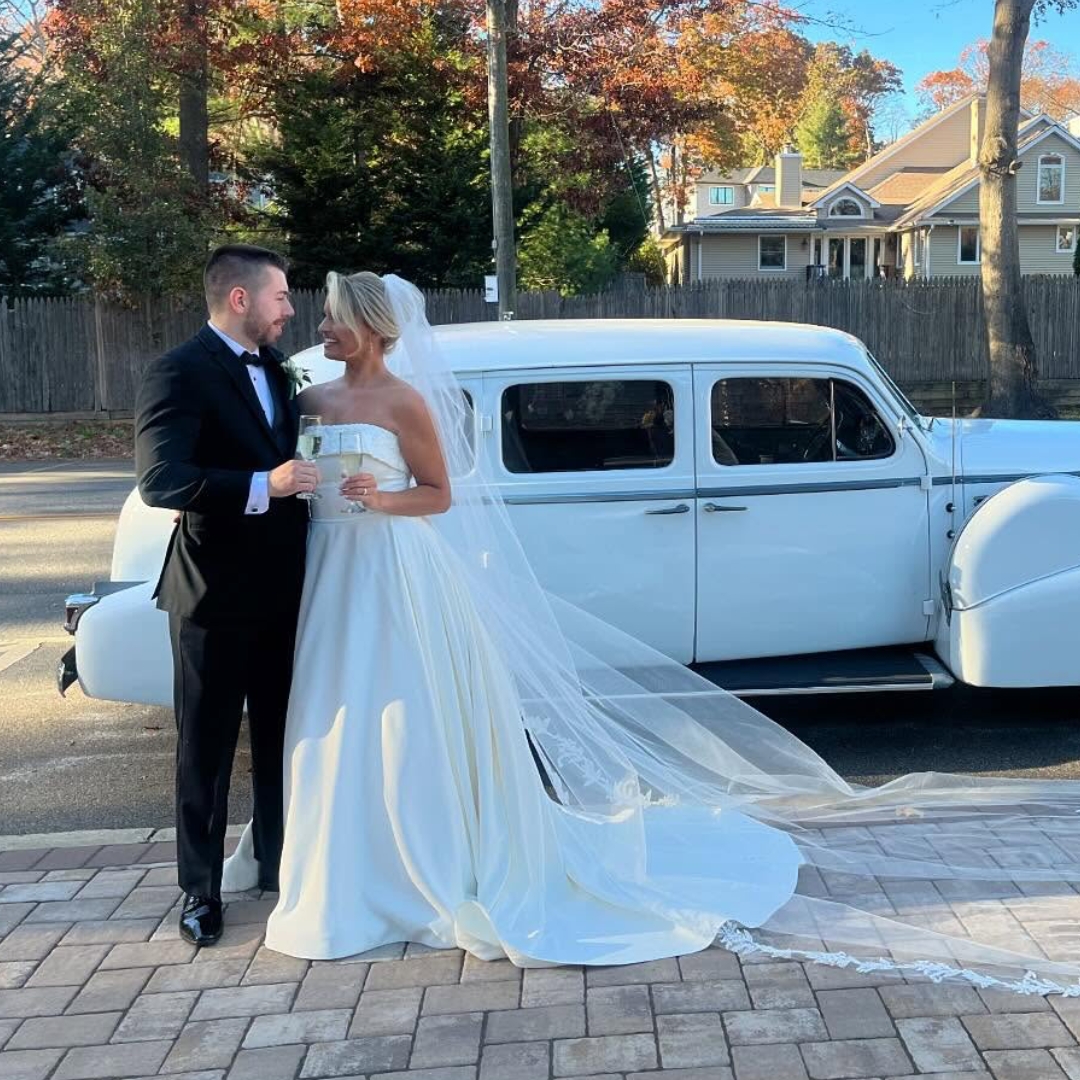 Newlyweds standing beside a vintage Camelot wedding car