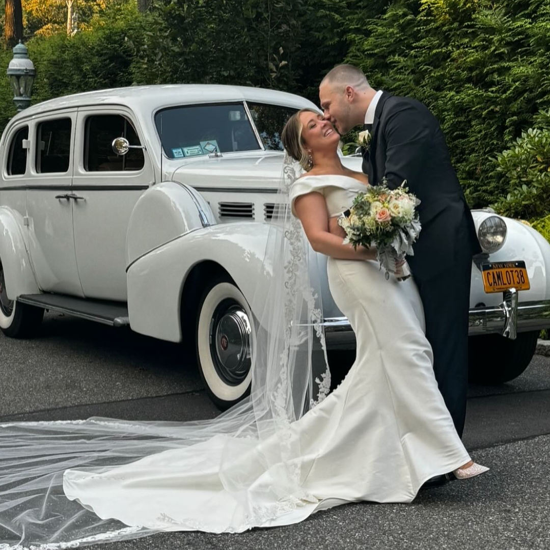 Bride and groom posing in front of a vintage Camelot car