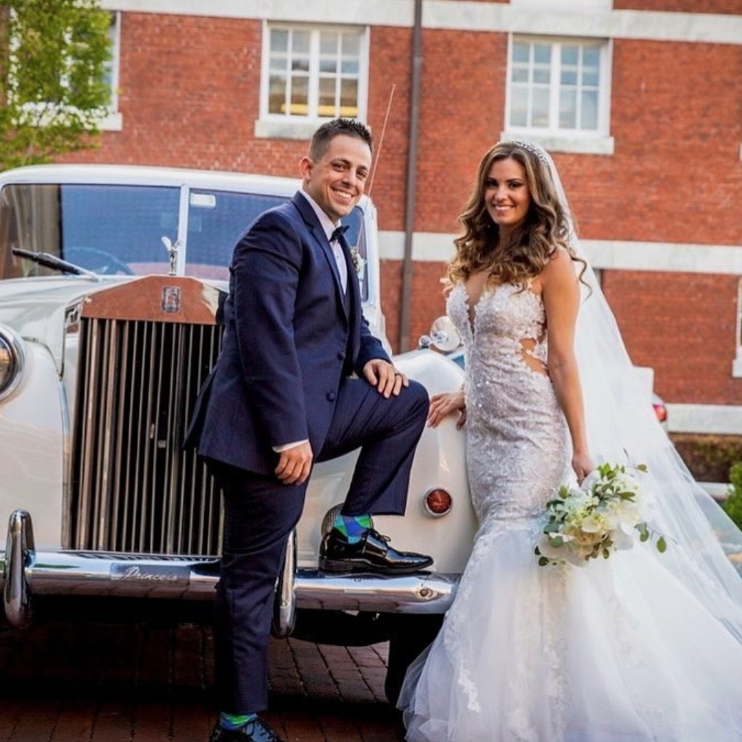Bride and groom posing with a white luxury wedding car